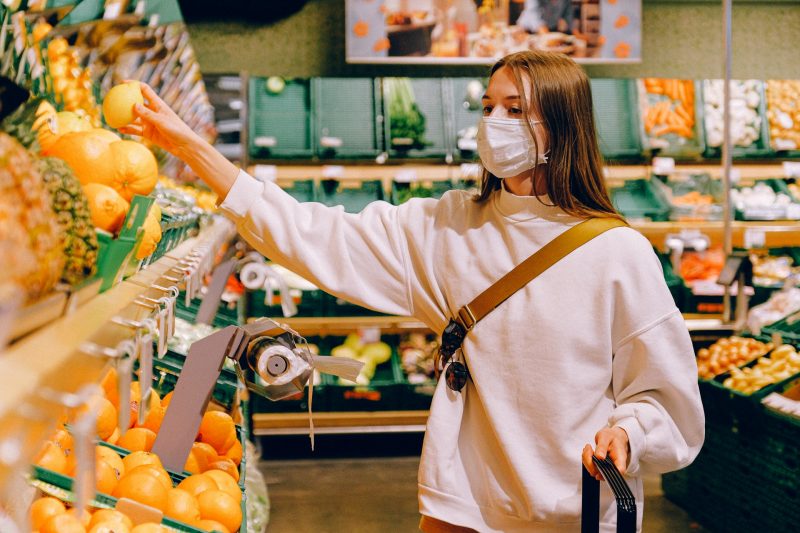 A woman wearing a face mask reaches for some fruit in a grocery store.