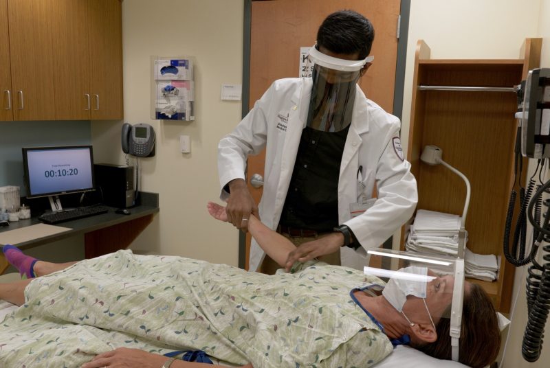 Student performs physical exam on a standardized patient while both wear PPE