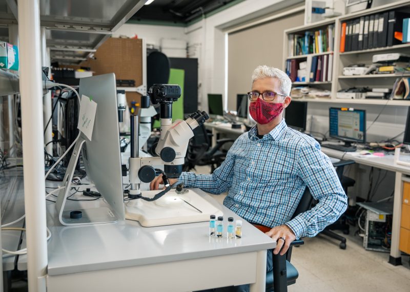 Jake Socha sits at his desk in front of a computer and a microscope, wearing his mask