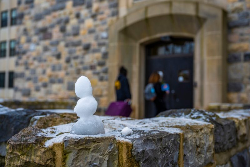 A tiny snowman sits on a ledge outside of a residence hall. 