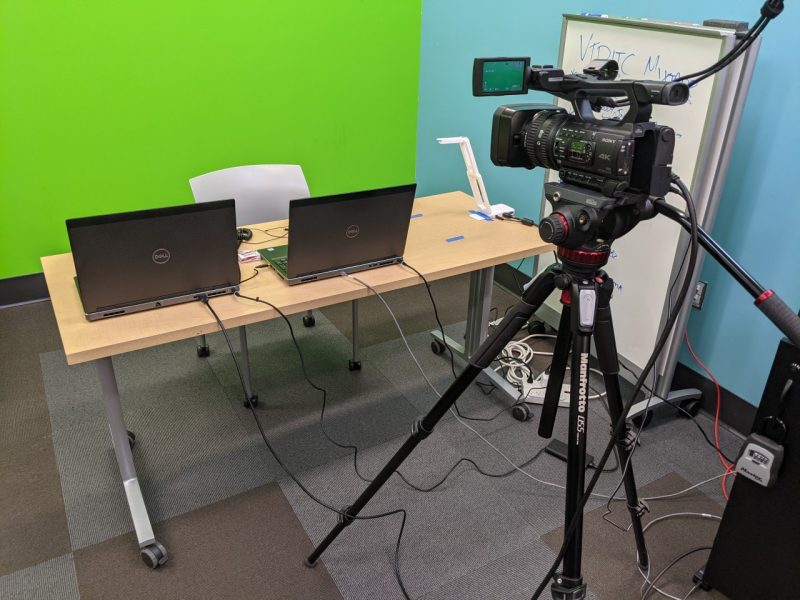 A camera on a tripod is pointed toward two laptops in from of a green screen. This is a typical broadcasting setup for the Archival Adventures show featuring documents from Special Collections and University Archives. 