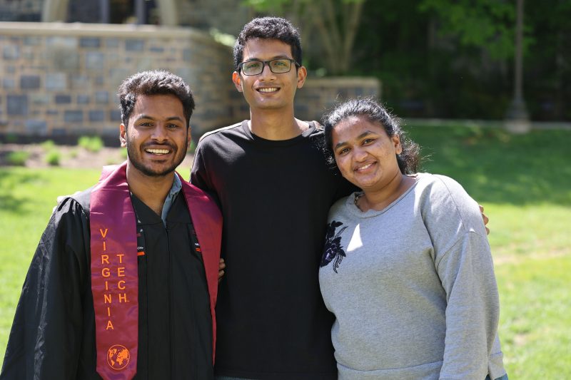 Three smiling 2021 graduates, one in graduation regalia, celebrate commencement and the end of the spring semester at a Cranwell International Center event.
