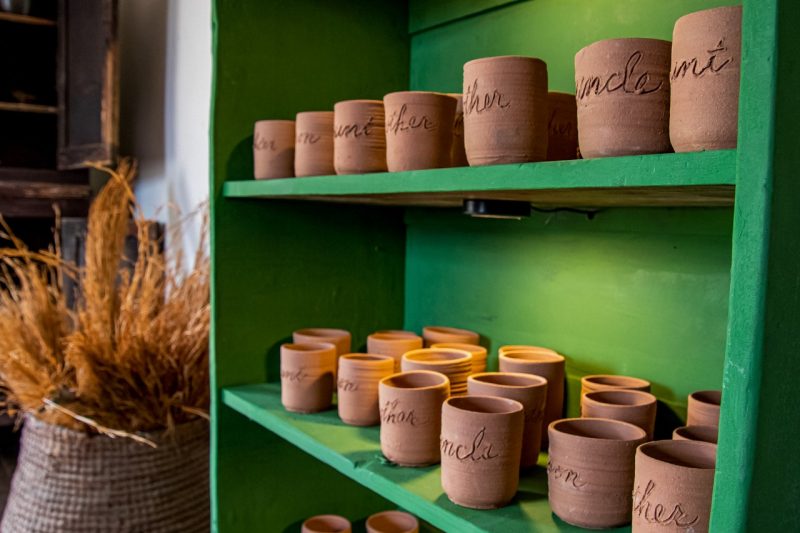 Rows of clay mugs sit on shelves in a bright green wooden cabinet.