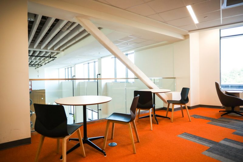 tables and chairs in an indoor collaboration space with bright orange carpet.