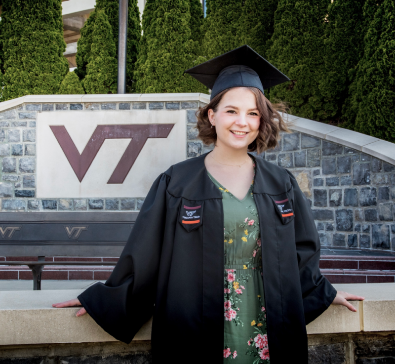 Ash VanWinkle, B.S. in Biochemistry, with a minor in Chemistry, stands in front of the large "VT" sign outside of Lane Stadium.