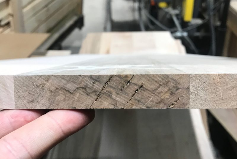 A piece of wood is held to show narrow cracks.