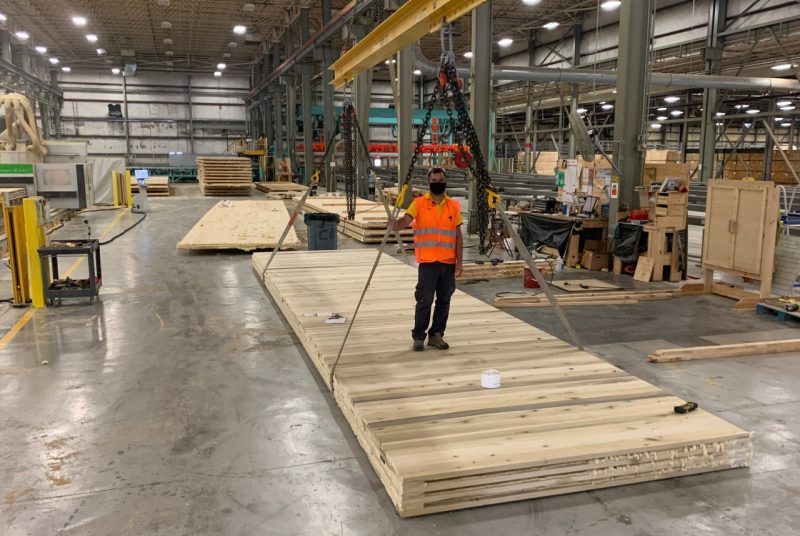 A person stands on a flat wood panel in a factory.