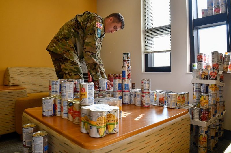 A cadet lifts cans of food from a table.