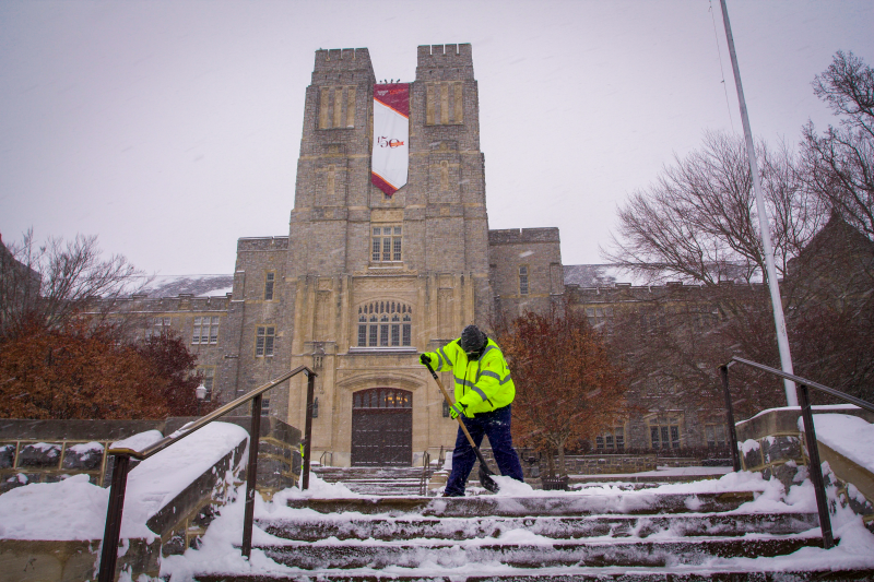 A person wearing high visibility clothing shovels snow off the Burruss steps 