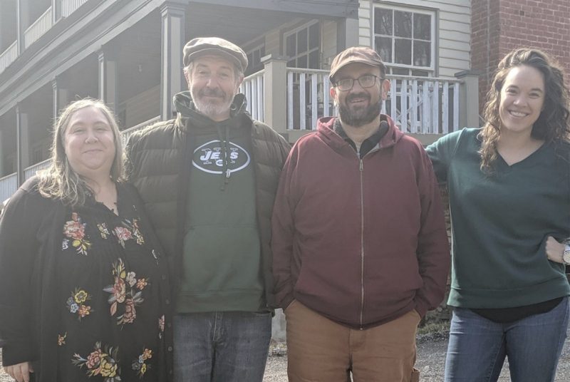Four writers pose side by side in front of an old house.