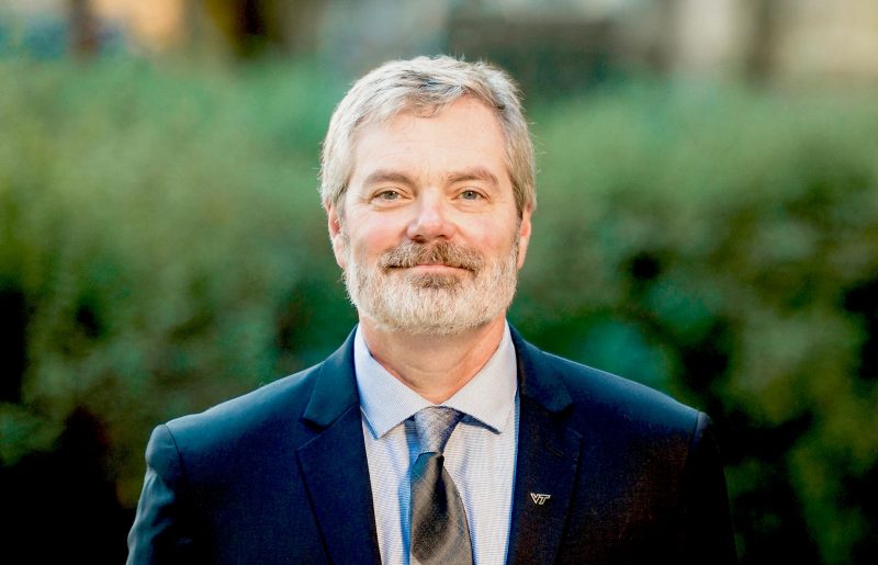 Steve Holbrook, professor and head of the Department of Geosciences, poses in a suit and tie, with a "VT" pin on his lapel