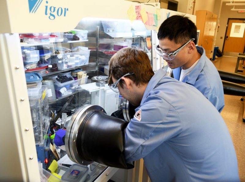 At foreground, Callum Connor, an undergraduate student in the Virginia Tech Department of Materials Science, works with highly sensitive chemicals used in the creation of lithium-ion batteries. His work requires gloves, then long rubberized arms inside a sealed argon-filled workstation. Inside the tank, a third pair of gloves is required. Next to Connor is Department of Chemistry postdoctoral researcher Zhengrui Xu, who is also a co-author on the paper. Photo for Virginia Tech by Natalee Waters.