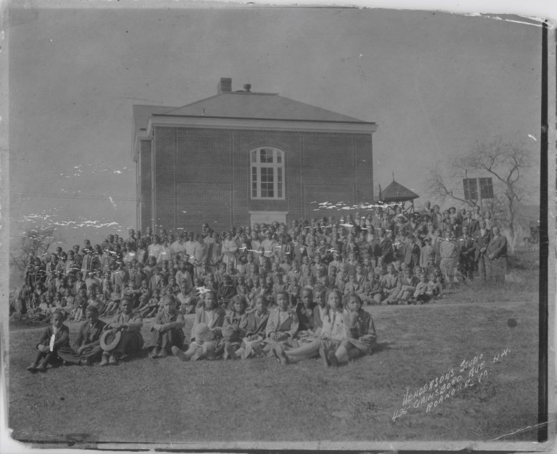In this historical photograph by Henderson Studio, a large group of students pose in front of a building at the Christiansburg Institute.