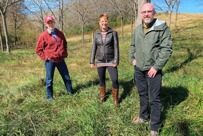Professors John Fike, Liesel Ritchie, and John Munsell stand together in a sparsely forested field.
