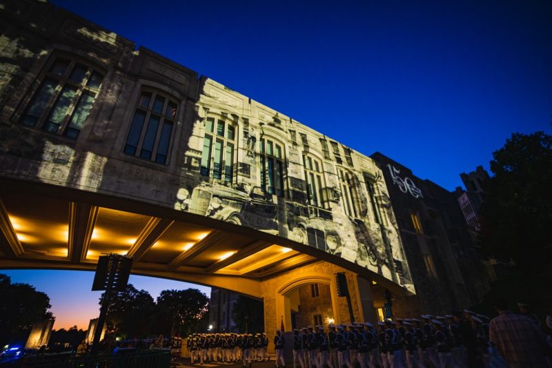 The Corps of Cadets marches beneath Torgersen Bridge, which features an image projected on it, as part of Homecoming fesitivities. 