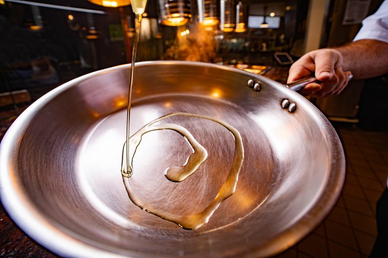 Oil swirls in a saute pan in a chef's hand.