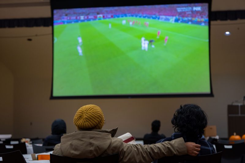 Two students watch the World Cup on a big screen.
