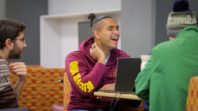 A student laughs while sitting at a study table with other students.