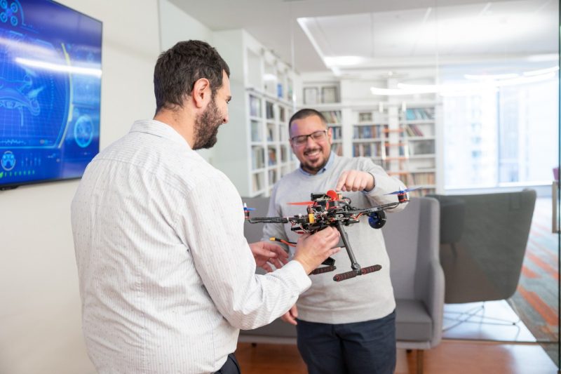 Walid Saad and student stand in library room and hold drone together