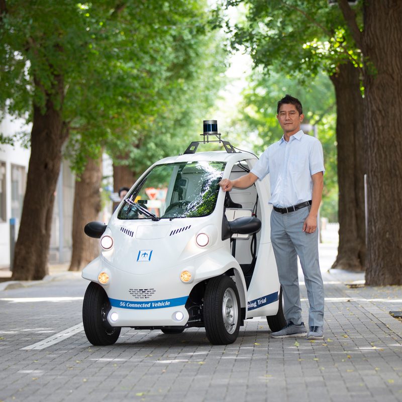 Professor stands next to autonomous smart car in the streets of Tokyo