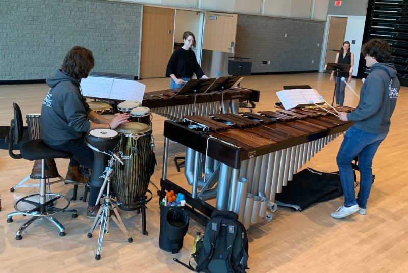 Three Virginia Tech percussion students, along with their instructor, rehearse on marimbas and drums in a large room.