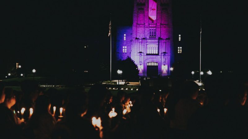 Burruss Hall is in purple as several people hold candles as part of Relay for Life