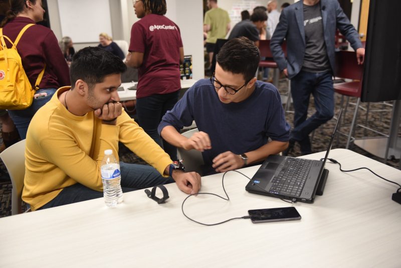 Two students troubleshoot IT issue at startup event.